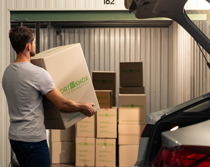 Person carrying a Fort Knox Storage box into a storage unit