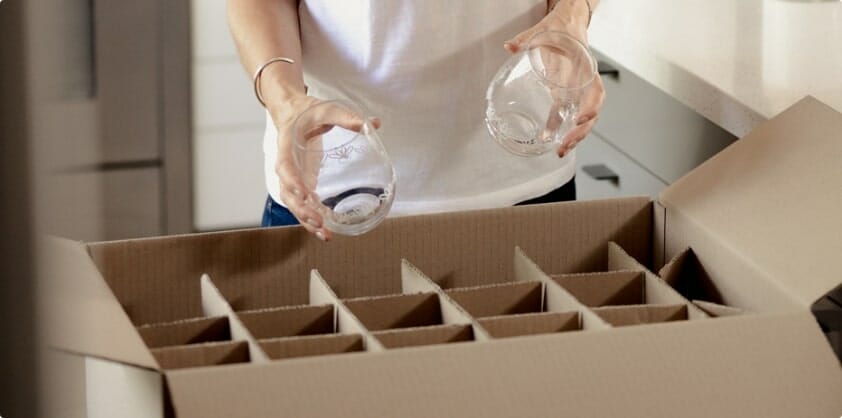 A person packing glasses into a storage box